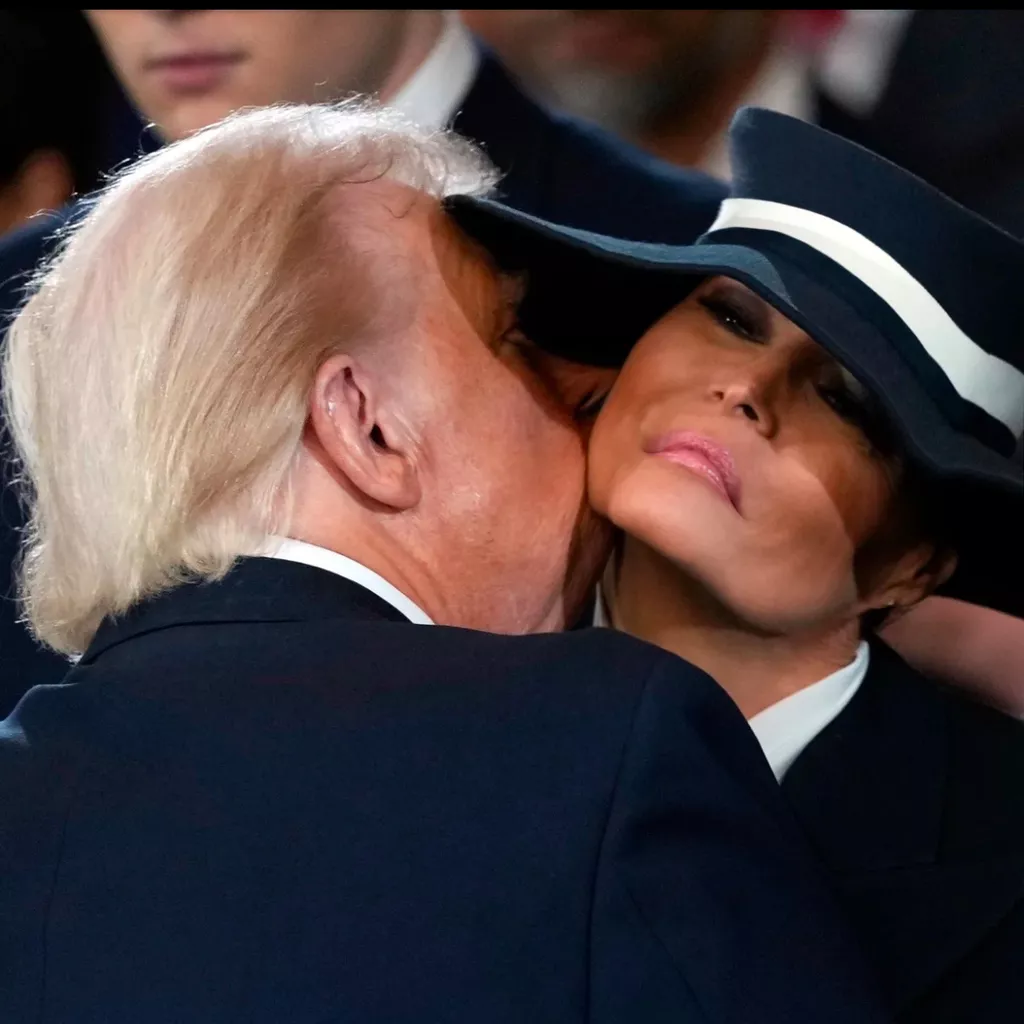 Melania, an elegant woman with long brown hair and a stylish outfit, is trying on various hats in a chic boutique. She is holding a large-brimmed sun hat, looking slightly dissatisfied.